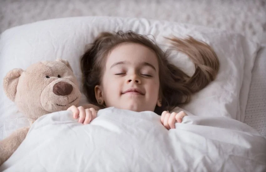 Niña durmiendo plácidamente en una cama blanca, ilustrando buenos hábitos para mejorar el sueño de los hijos.