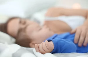 Madre durmiendo junto a su bebé en una cama, practicando colecho seguro