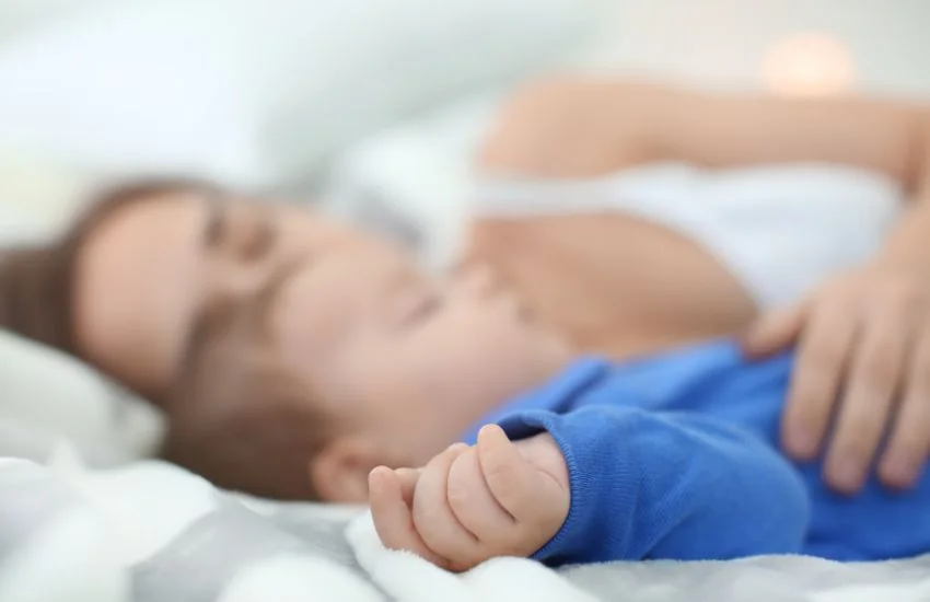 Madre durmiendo junto a su bebé en una cama, practicando colecho seguro